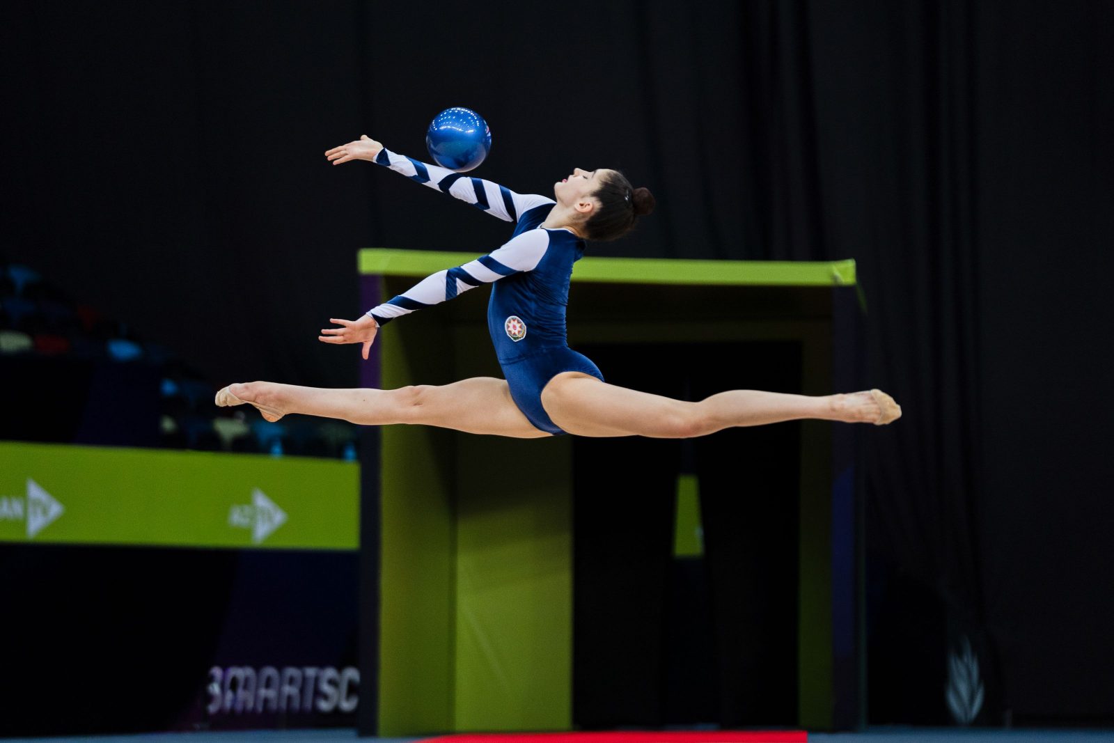 Gimnasta de gimnasia rítmica en pleno salto con la pelota durante una competición